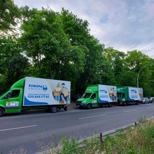 Drei Umzugsfahrzeuge von Europa Umzüge in einer Reihe auf einer Allee